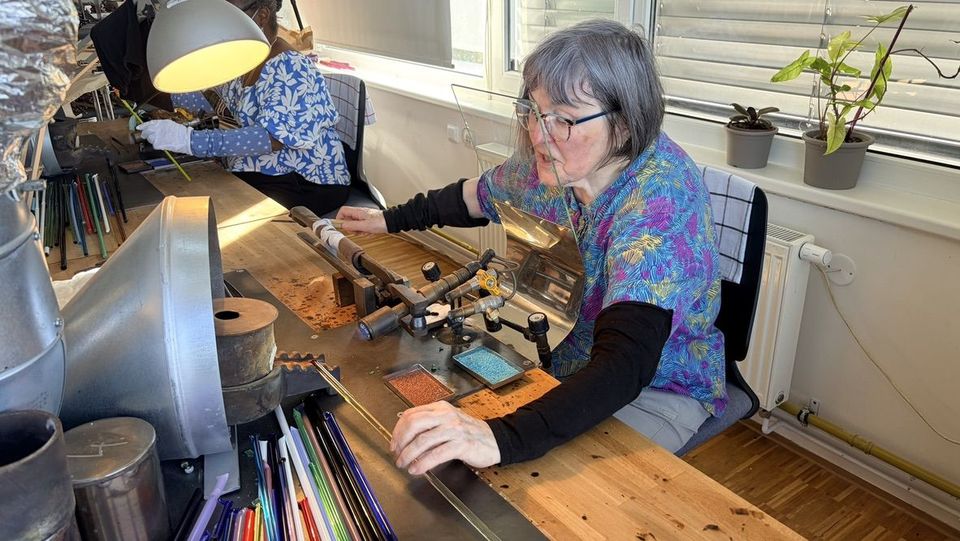 Lampworker with grey hair shaping a glass cabochon