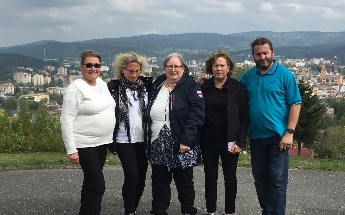 A tour group smiling at a hilltop viewpoint above a Czech town