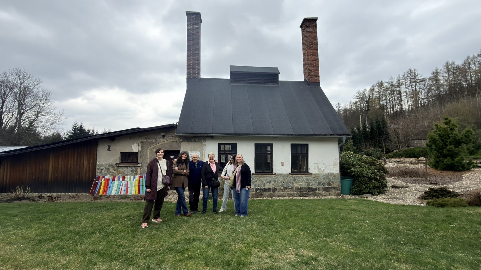 Visitors outside a traditional cottage glass factory with tall brick chimneys near Jablonec