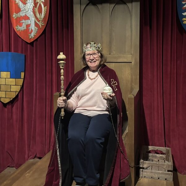 Eileen Ranson wearing a crown and robe on a throne, holding a sceptre and orb