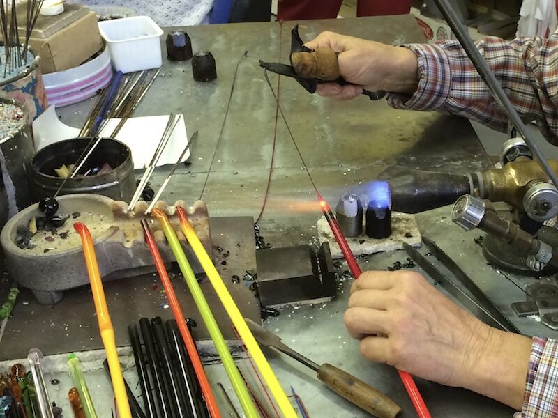 Hands shaping glass rods in a lampwork flame
