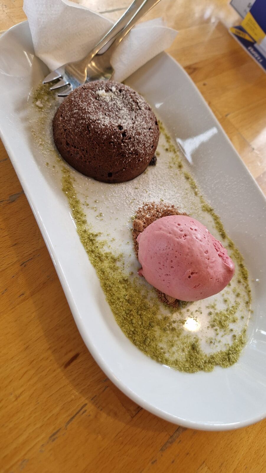 Warm chocolate fondant dusted with sugar, with a scoop of raspberry sorbet on a pistachio crumb