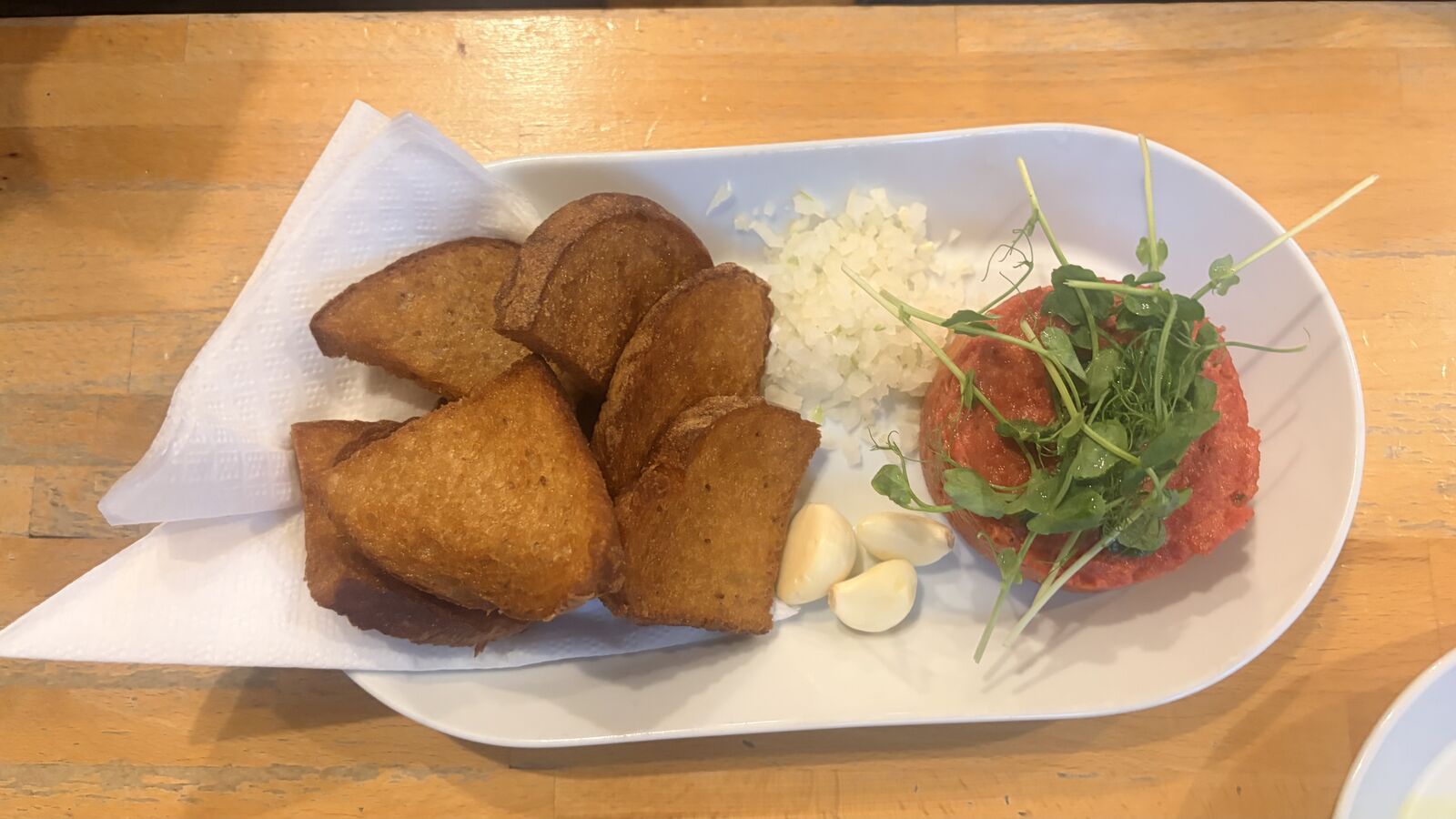 Czech beef tartare topped with pea shoots, served with fried toast, garlic cloves and chopped onion