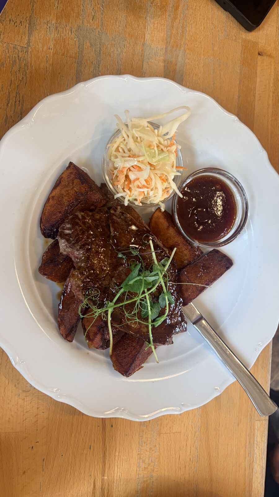 Glazed steak with potato wedges, a pot of coleslaw and barbecue sauce